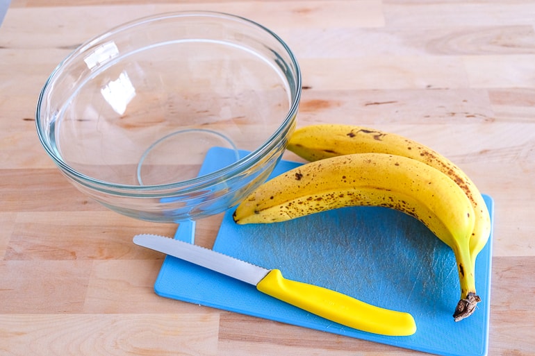 bananas on cutting board with bowl and knife vegan buckwheat banana pancakes