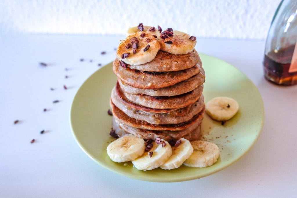 stacked pancakes on green plate with sliced bananas