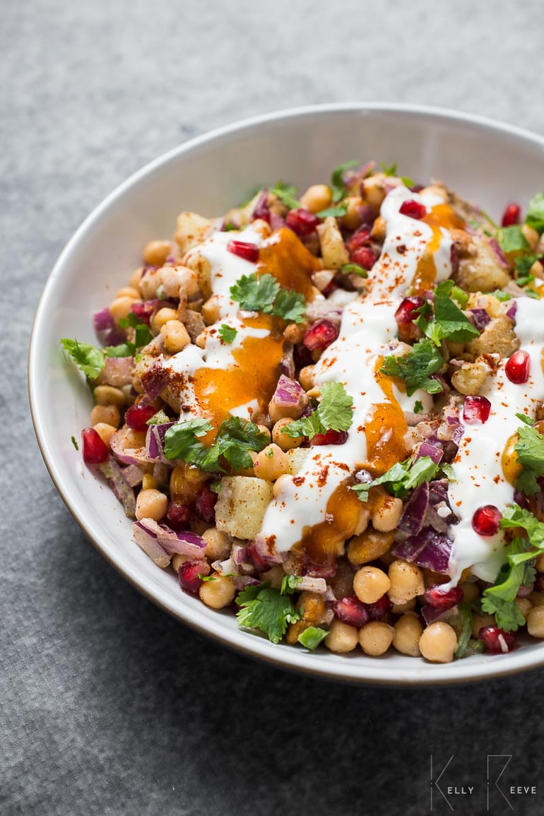 Chickpea salad with pomegranates, greens and dressing in white bowl