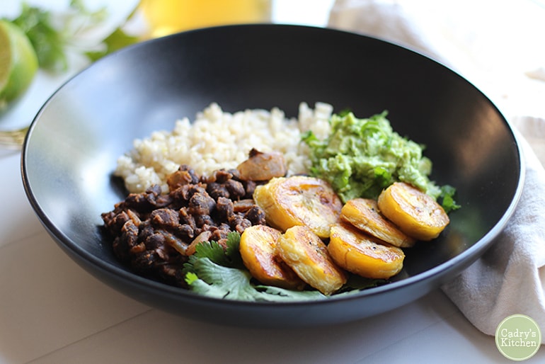 Blackbeans, rice, plantains and guacamole in black bowl
