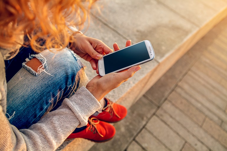 Woman with jeans and curly hair looking at a smartphone in her hand couples apps