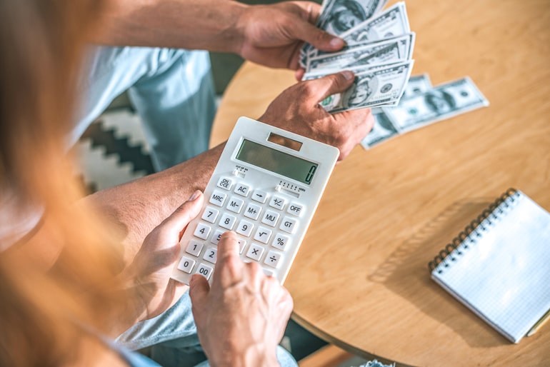 Woman holding white calculator with man in background holding money bills