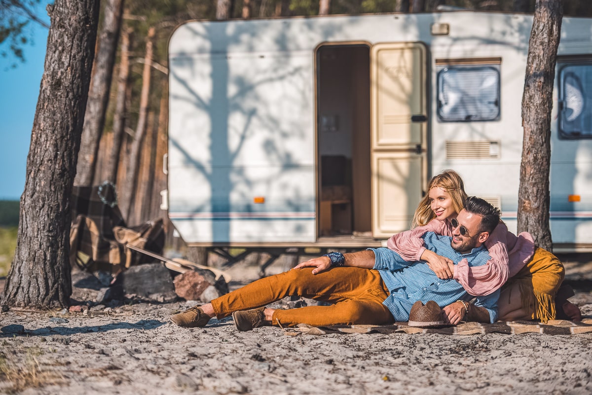 Couple hugging each other on ground in front of white trailer and trees couples bucket list