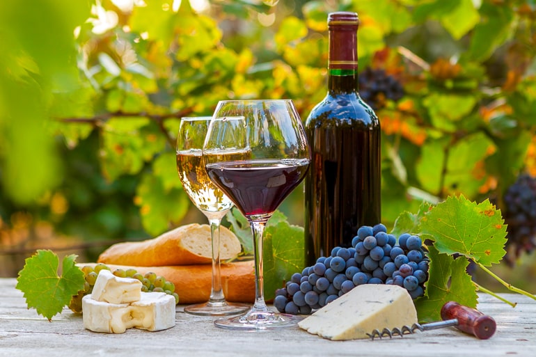 Glasses and bottle of wine with cheese bread and grapes on table