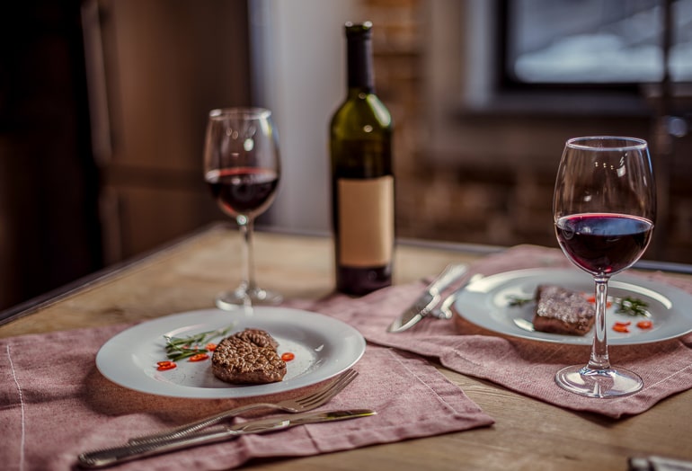 two plates with steak and wine glasses with bottle behind on table date night at home ideas
