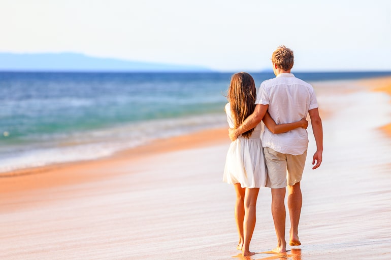 couple wearing white walking together down sandy beach
