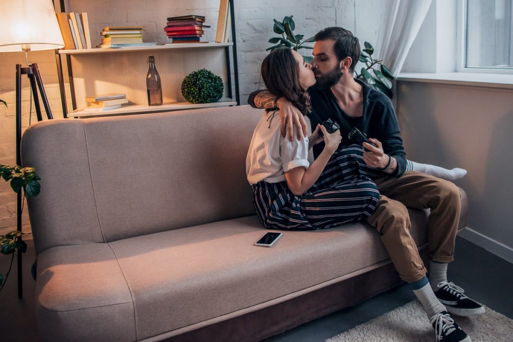 couple sitting in couch holding controllers while kissing