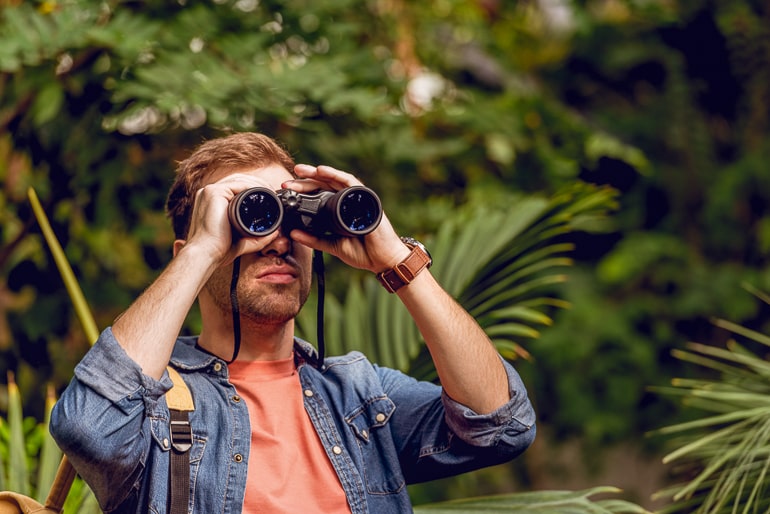 man standing looking through binoculars