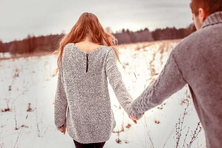 woman walking holding hand of man with snow on ground