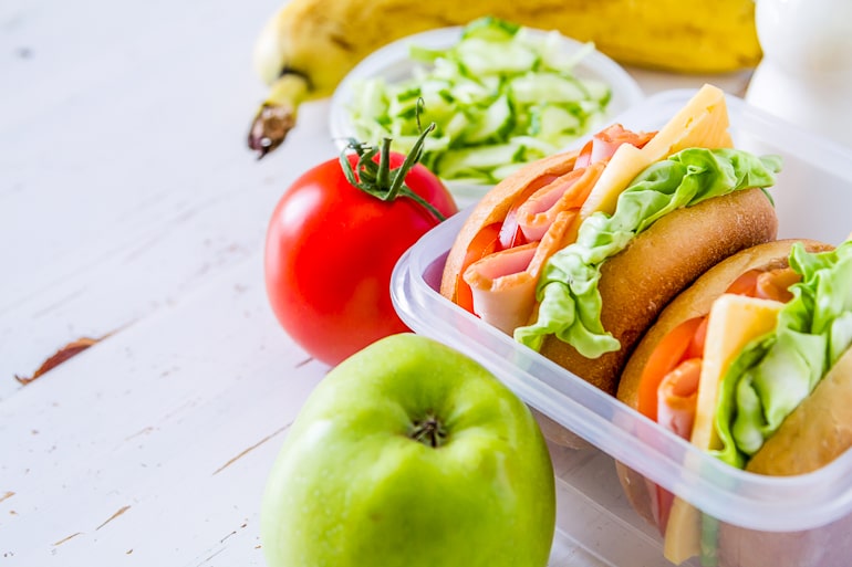 Lunchbox with sandwiches and apple tomato and banana next to it