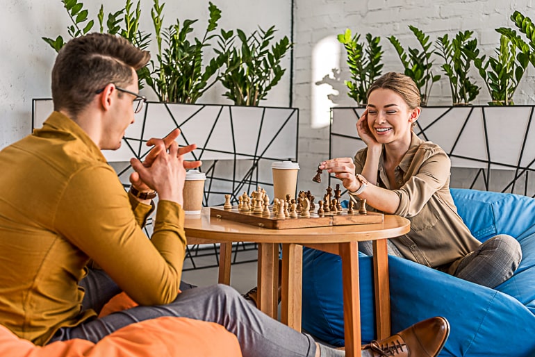 Man and woman sitting on beanbags and playing chess on small brown table