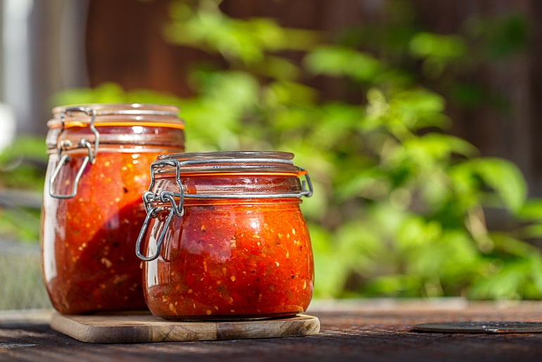 Two jars of homemade tomato sauce with green background
