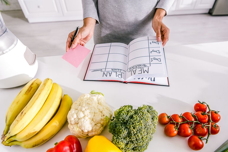 Woman holding meal plan table on counter with fruit and vegetables next to it