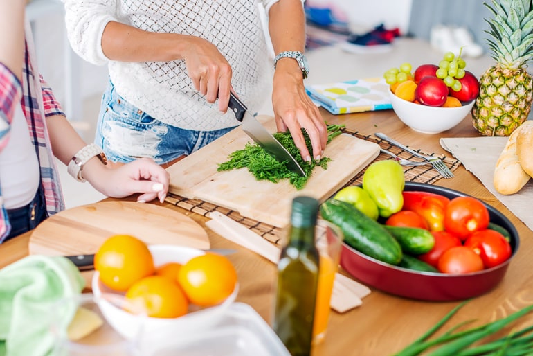 woman cutting herbs on cutting board with fruit and vegetables next to it