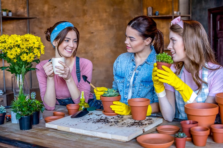 Three woman looking at each other while holding pots and plants in their hands gardening