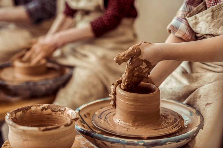 Hands shaping clay on pottery wheel