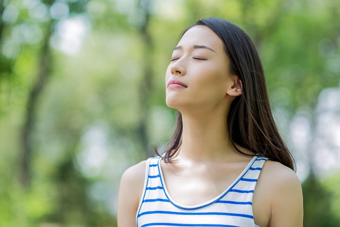 woman with striped top breathing outside in forest how to stop an anxiety attack