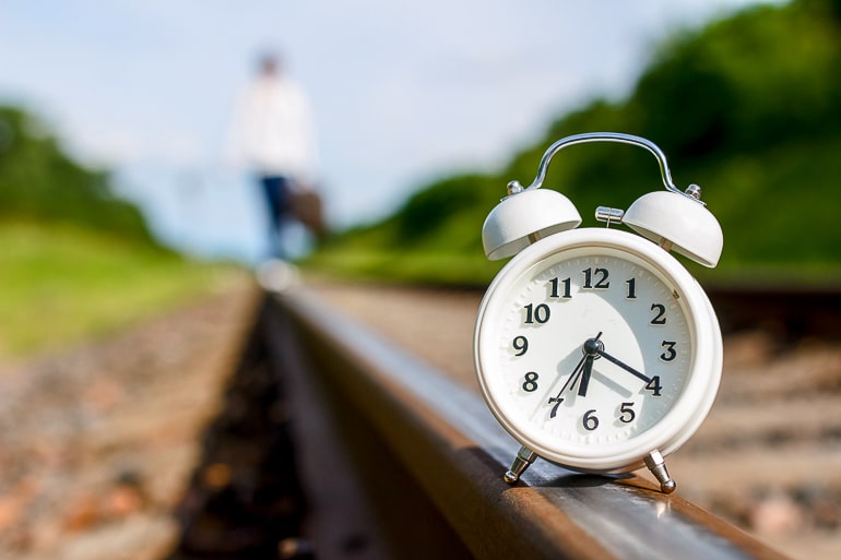 White clock sitting on train tracks with blurry background