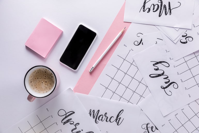 calendar pages on desk with phone and coffee mug