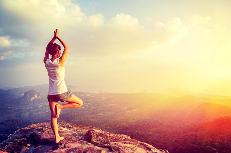 woman in pose on cliff with sun importance of yoga in modern life