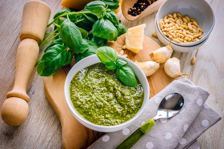 green pesto in white bowl with ingredients around on counter