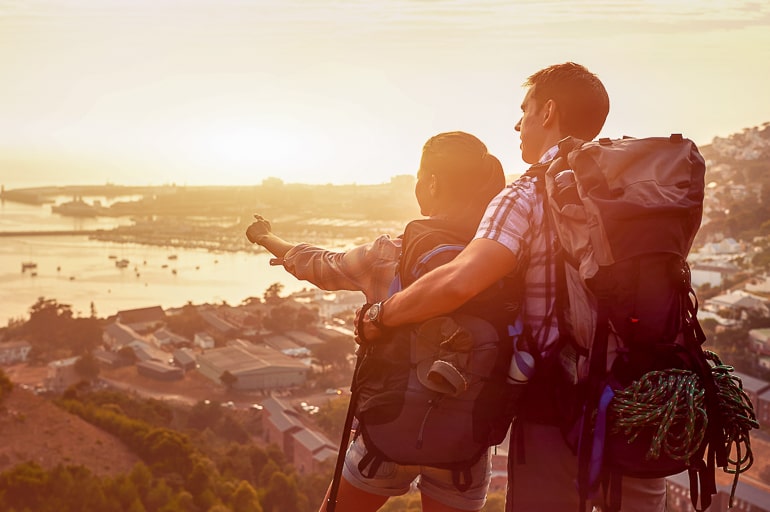 couple travelling with backpacks looking at sunset from cliff