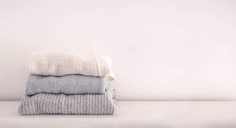 small stack of shirts folded on white ground with white wall living in the present