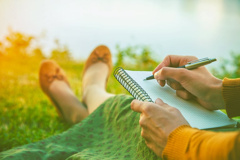 Woman sitting on grass with notebook and pen in hand
