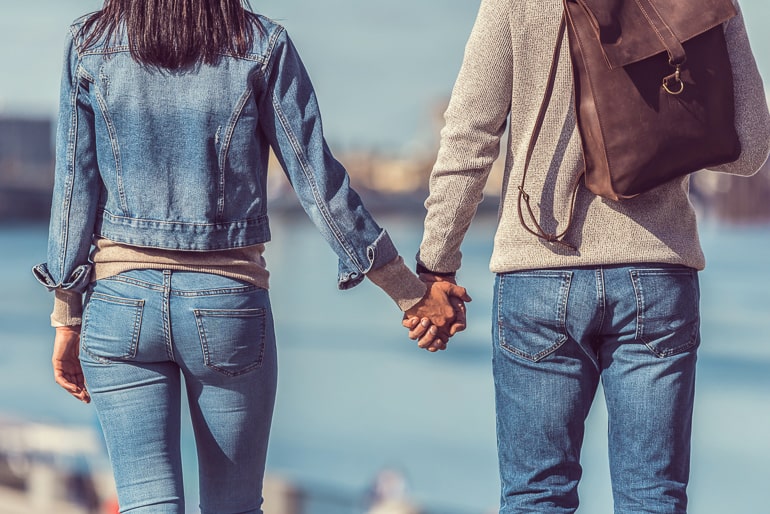 Back of man and woman in jeans holding hands