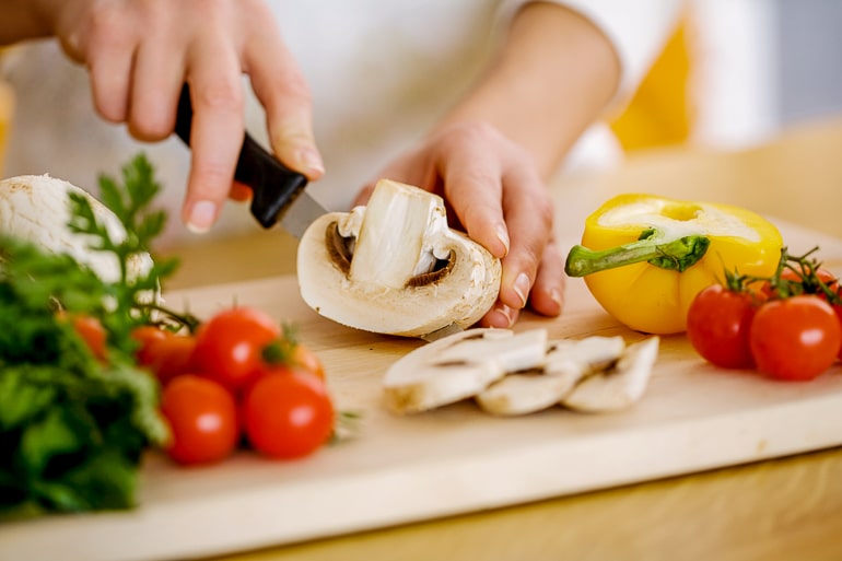 hand holding knife cutting mushroom on wooden cutting board