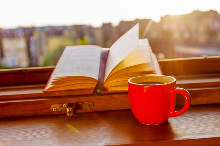 open book with orange mug beside on windowsill