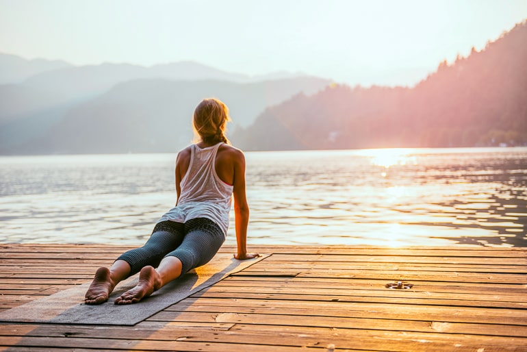 woman doing yoga pose on wooden dock with sun in front new years resolution ideas