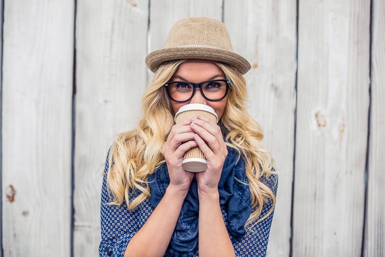Blonde woman with hat gasses holding a coffee cup in her hand