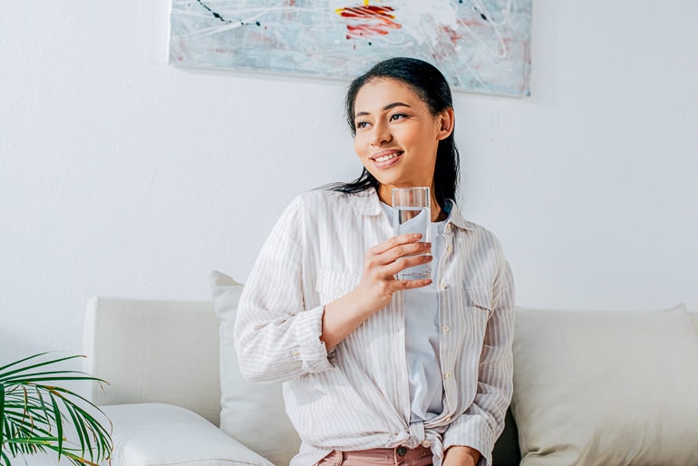 Woman looking to the side while holding a full glass of water in her hand