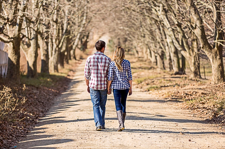 Man and woman in relationship holding hands walking on path lined with trees