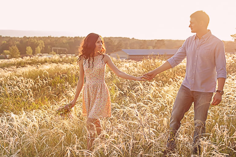 Couple walking in field holding hands and looking at each other separation anxiety