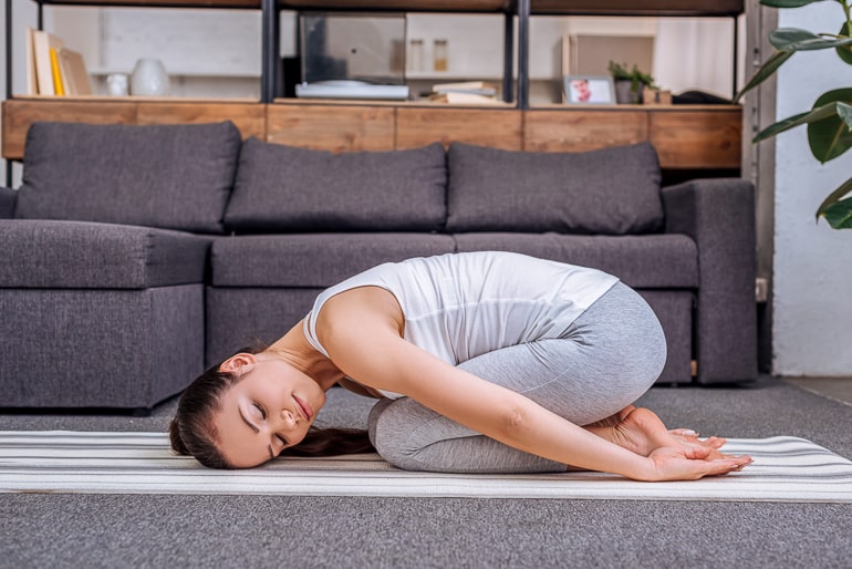 Woman in living room on yoga mat doing childs pose