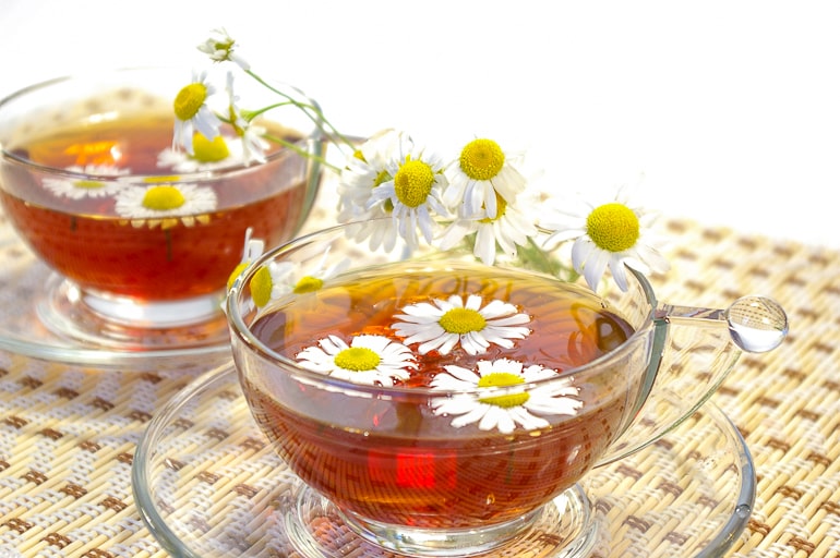 chamomile flowers in clear tea mug on clear plate