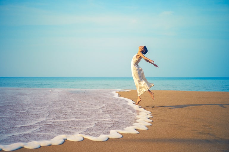 Woman jumping on beach with water and sand underneath her