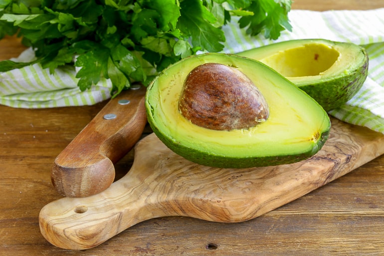 green halved avocado with pit on wooden cutting board