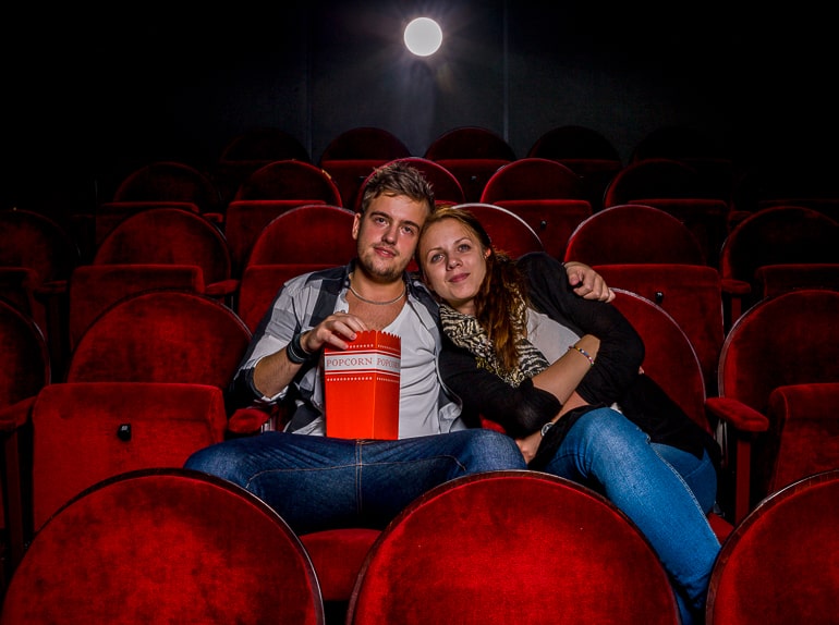 man and woman sitting in movie theatre on red chairs