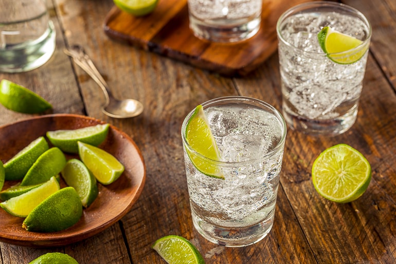 two short glasses of gin and tonic with limes in wooden table