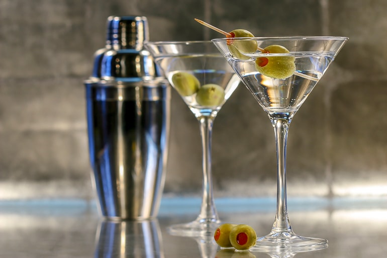two martinis with olives and a silver shaker behind