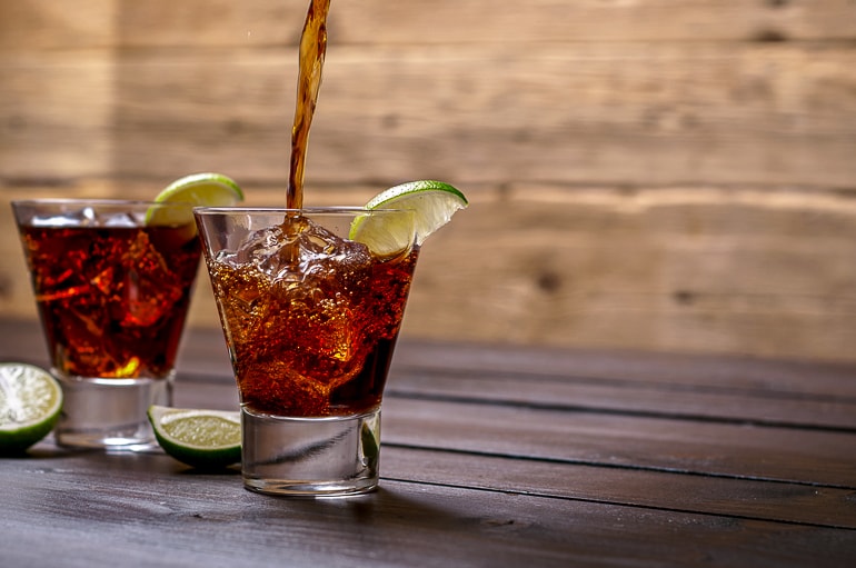 two short glasses with rum and coke with slices of limes