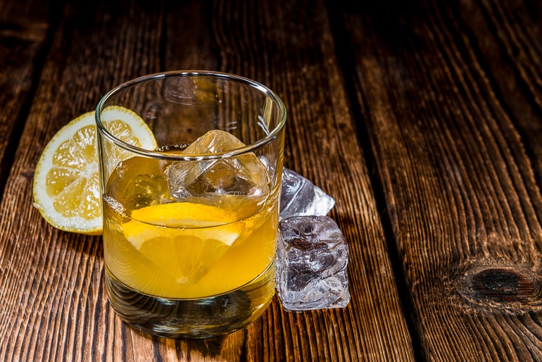 cloudy drink with ice and orange in short glass in wooden table whiskey sour