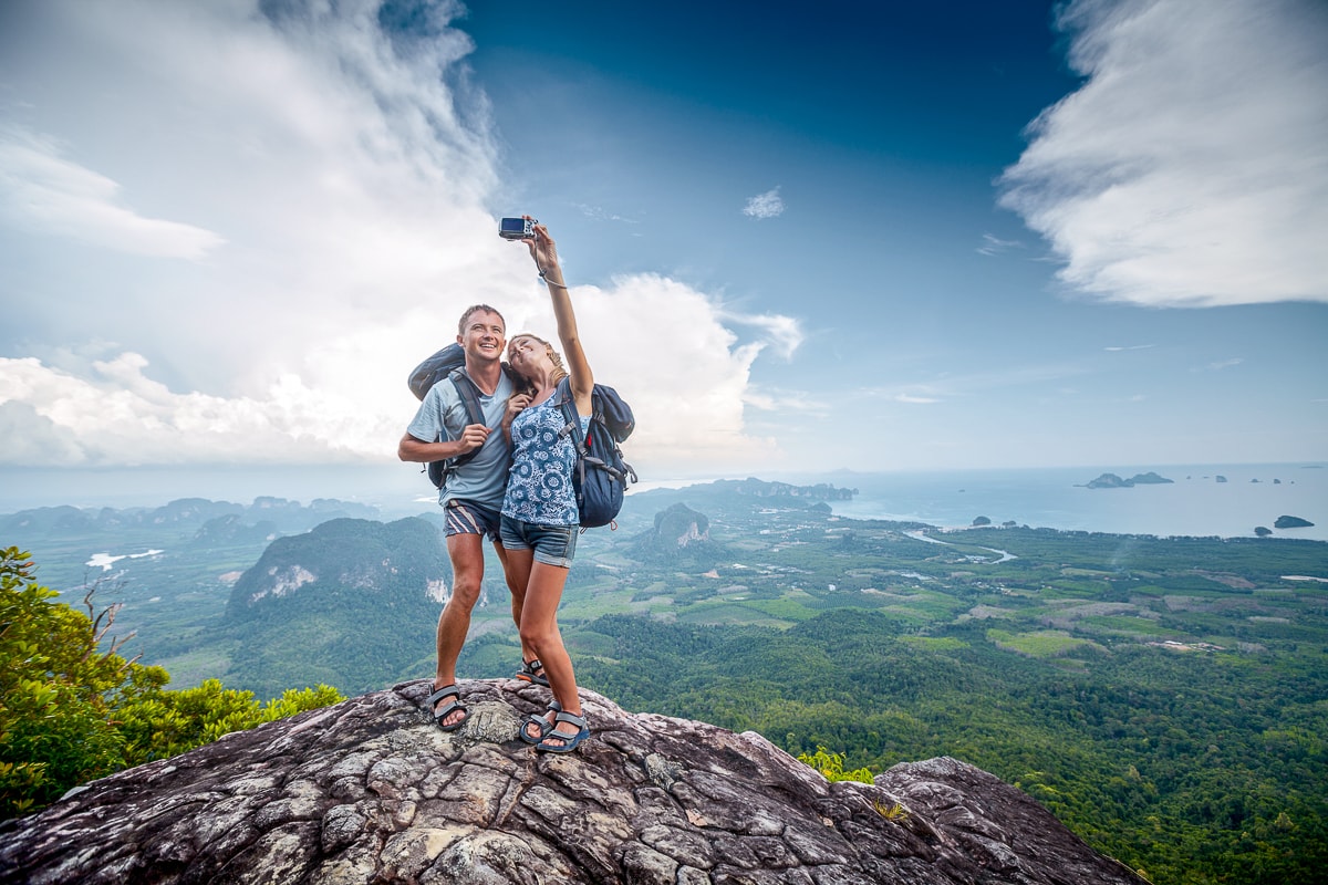 Couple with backpacks taking photo of themselves on rock captions for pictures of yourself