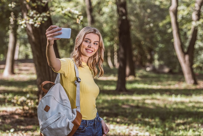 Woman in yellow top with backpack taking photo of herself
