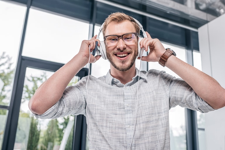 Man with glasses wearing white headphones and laughing