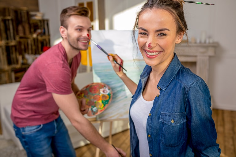 Man and woman holding paint brushes and having paint on their nose