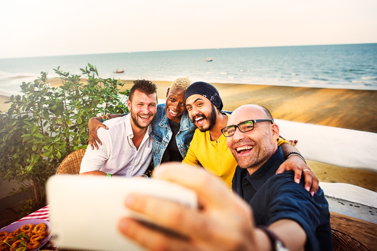 group of men taking selfie with beach and ocean in background
